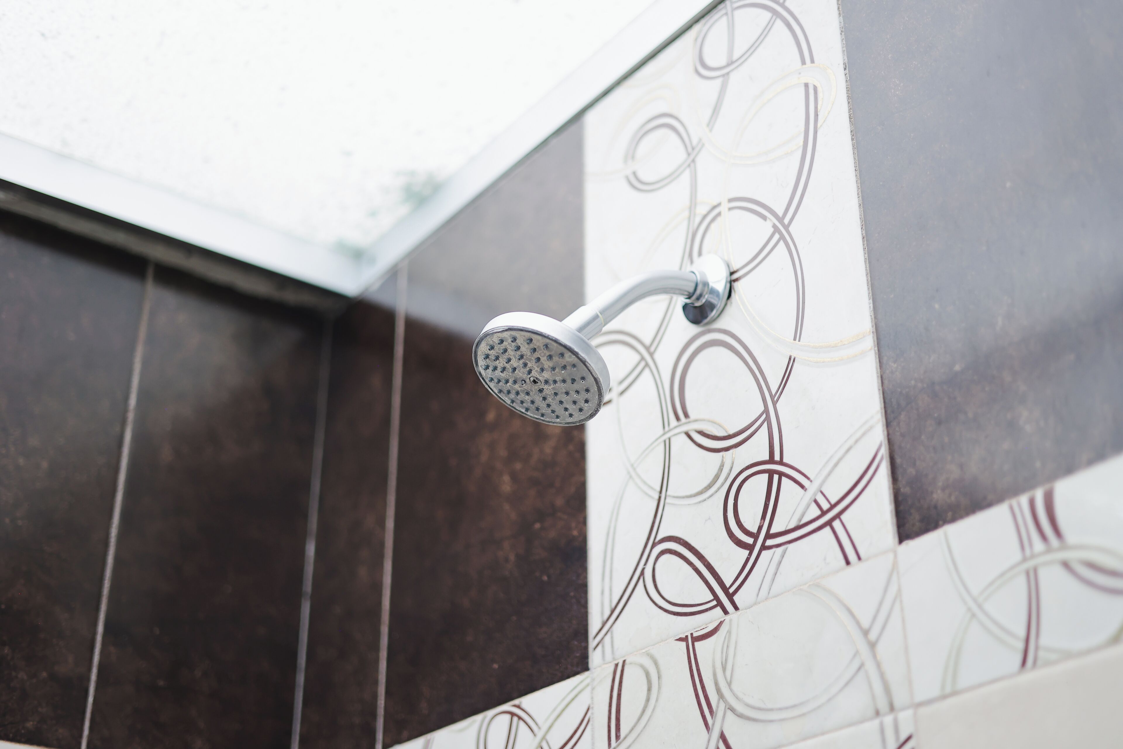 Un cabezal de ducha con diseño curvo, instalado en una pared con baldosas decorativas.