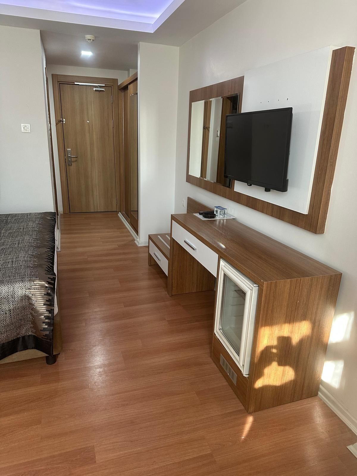 A bedroom with a bed, a wooden dresser, a vanity, a mirror, and a TV.