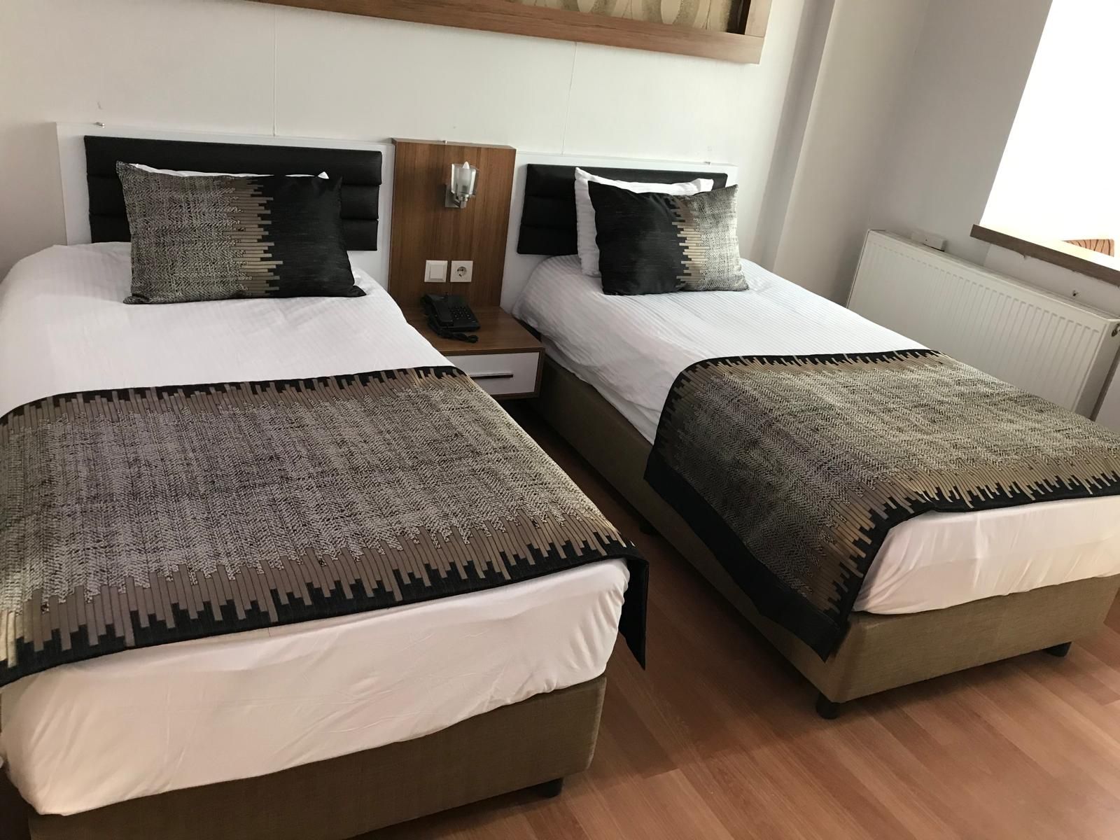 A double bed with a headboard, a bedside table with a lamp, and a window with blinds.