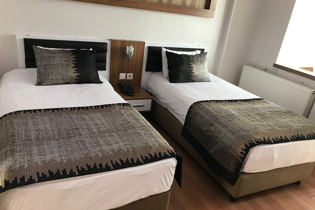 A double bed with a headboard, a bedside table with a lamp, and a window with blinds.