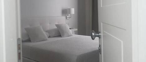 A modern bedroom with a bed, bedside table, lamp, and a door.