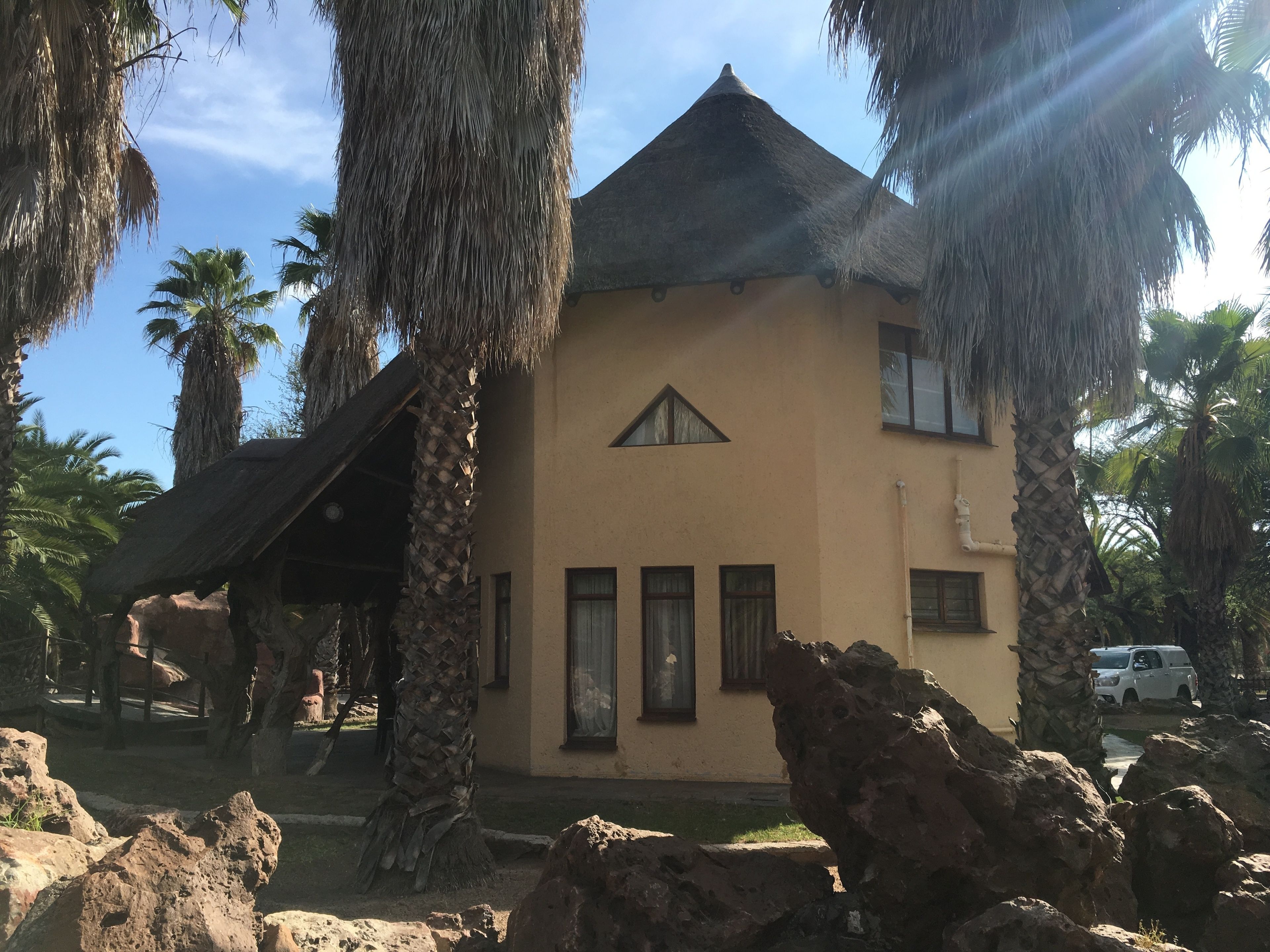 Un edificio con tetto di paglia, circondato da palme e rocce.