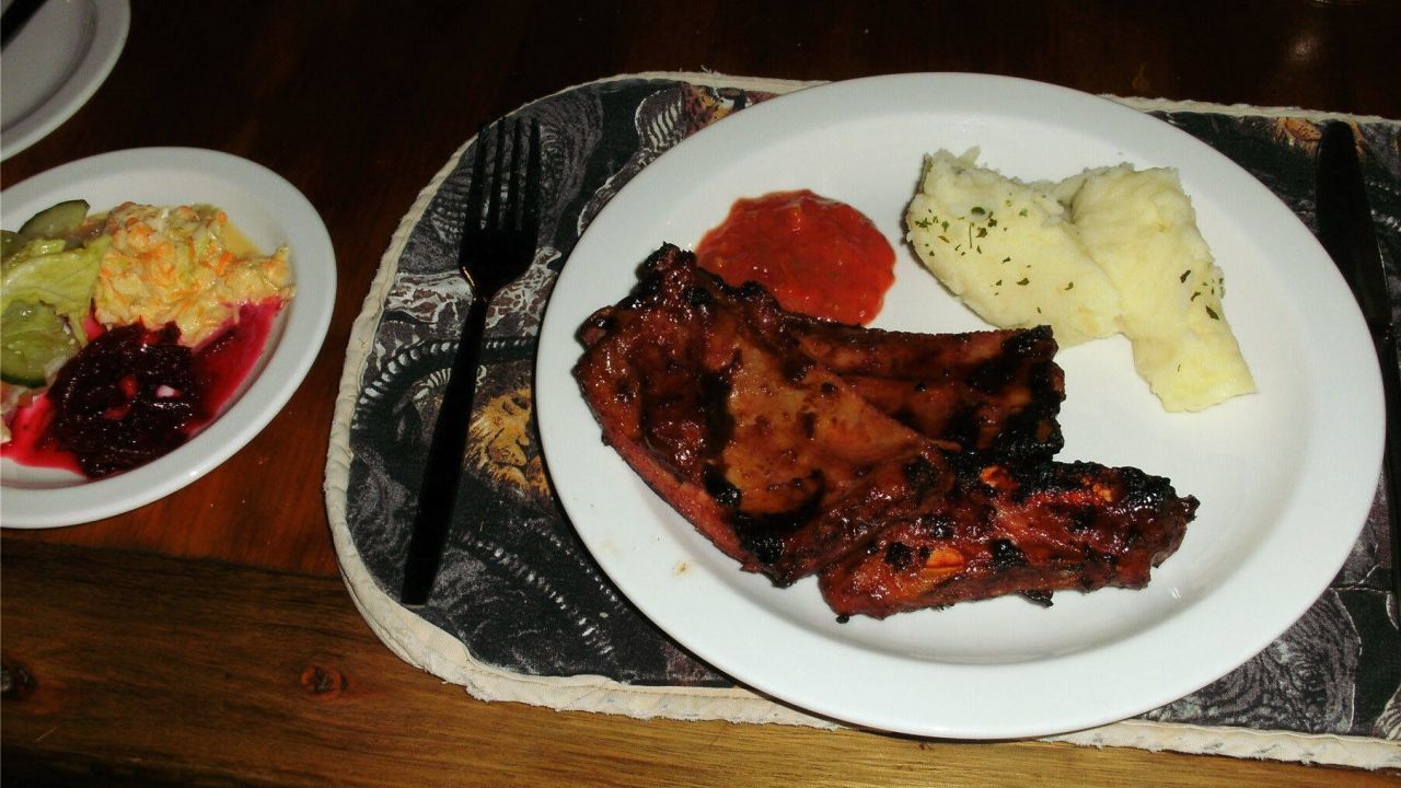 A plate with grilled meat, mashed potatoes, and a side of pickles and cranberry sauce.