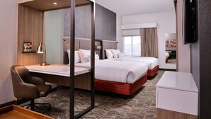 Una habitación de hotel con escritorio, dos camas, televisión y espejo.