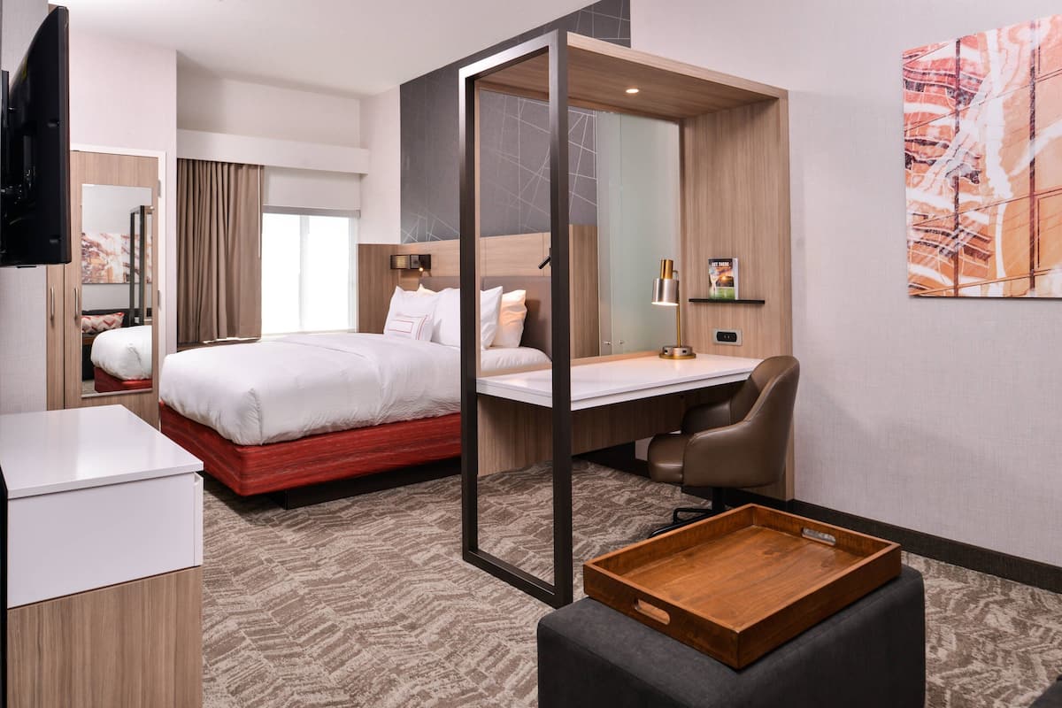 A modern hotel room with a bed, desk, chair, and a small wooden table.