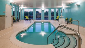 Una piscina con solárium de azulejos, un vestuario con sillas y vistas amplias a través de grandes ventanales.