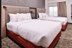 Habitación de hotel con dos camas, un cabecero moderno, un ventanal grande y vistas de la ciudad.