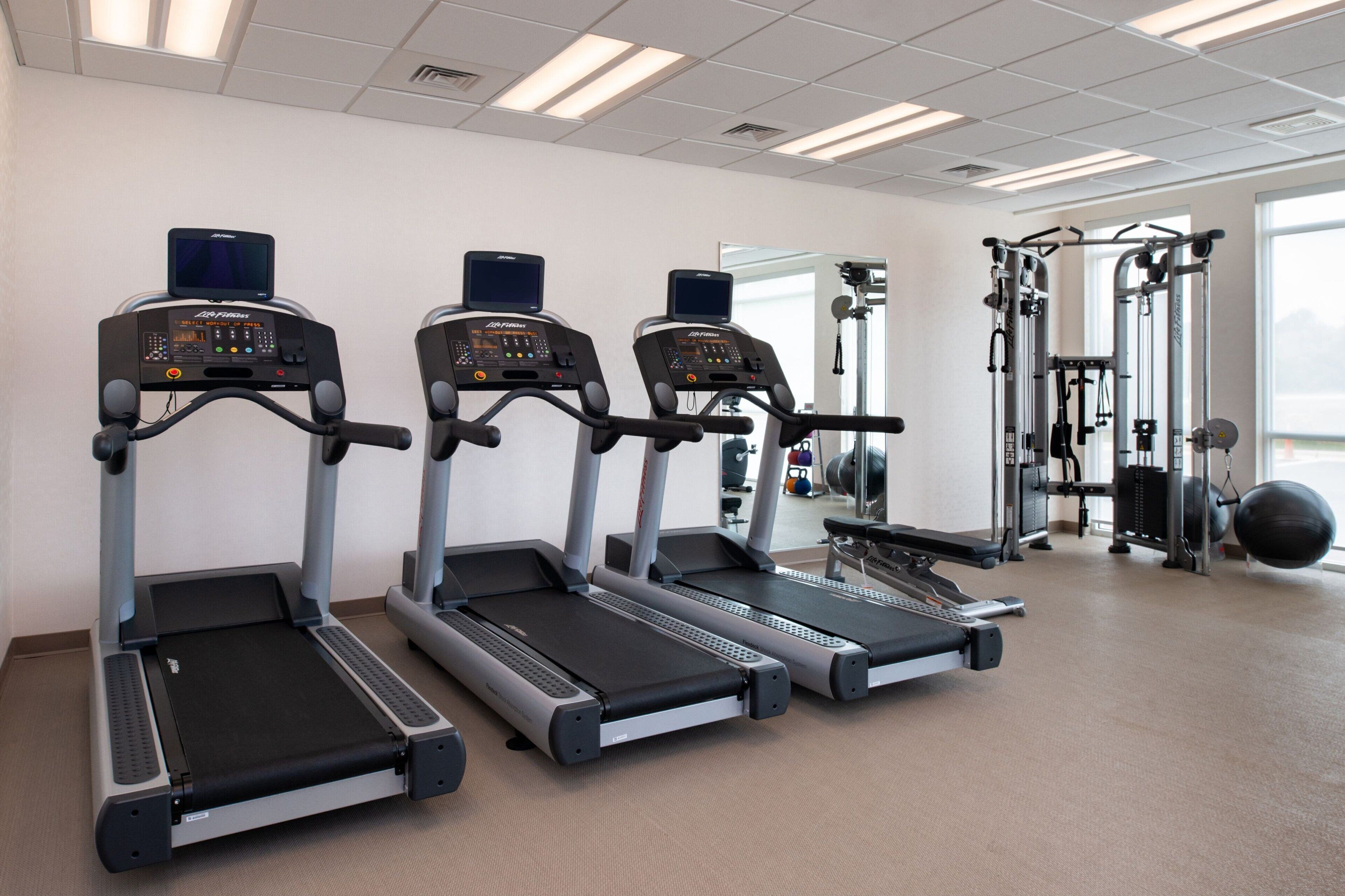 Three treadmills, a weight machine, and a large exercise ball in a gym with a plain wall and a door leading outside.