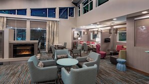 Un hall d’hôtel moderne doté d’une cheminée, d’un espace salon et de grandes fenêtres.
