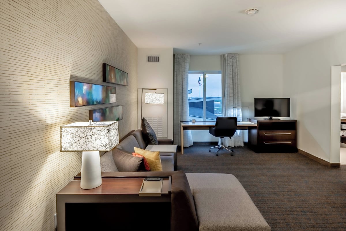 A hotel room with a sofa, a desk, a TV, and a window with a view of a building.