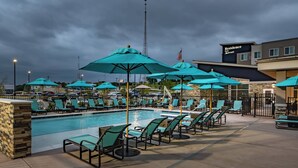 Un espace piscine avec des chaises longues et des parasols, un bâtiment du Marriott Residence Inn et un ciel dégagé.
