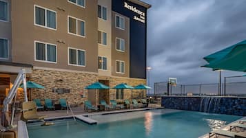 Una piscina al aire libre, sombrillas, sillones reclinables de piscina