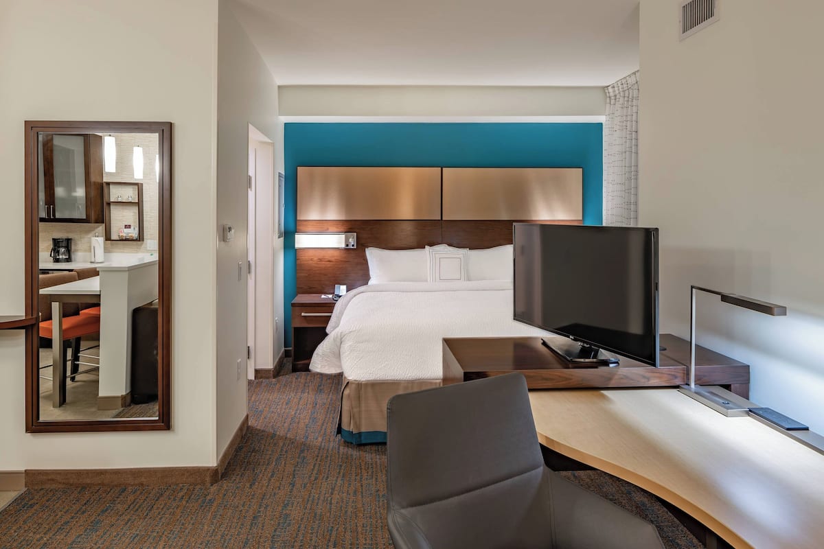 A hotel room with a bed, a desk, a chair, a TV, and a mirror.