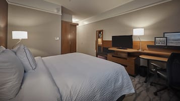 A hotel room with a large bed, a desk with a computer, a TV, and a chair.