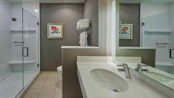 Un baño moderno con cabina de ducha de vidrio, lavamanos blanco con encimera de cristal y un espejo grande.