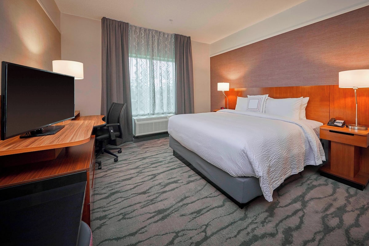 Habitación de hotel con cama, escritorio, televisión y lámparas.