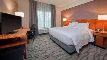 A hotel room with a bed, desk, television, and lamps.