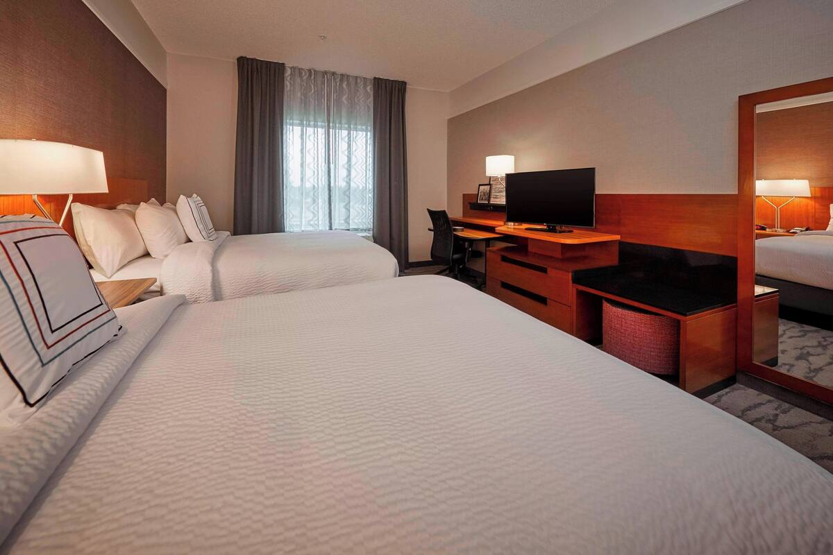 Habitación de hotel con dos camas, un escritorio con televisor y un espejo grande.