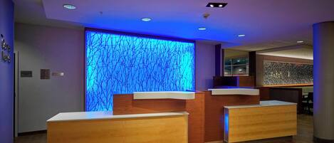 A reception area with wooden reception desks and a wall with a blue illuminated tree design.