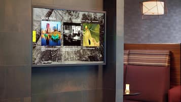 Un intérieur moderne doté d’un grand écran numérique affichant du contenu provenant des réseaux sociaux, d’un espace salon avec un banc rembourré et une petite table, ainsi que d’un luminaire suspendu aux formes géométriques.