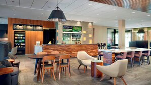 Un moderno vestíbulo de hotel con zona de bar, asientos y una pantalla de televisión.