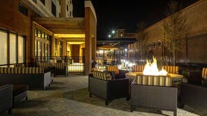 Un espacio al aire libre con mobiliario de mimbre y una chimenea central.