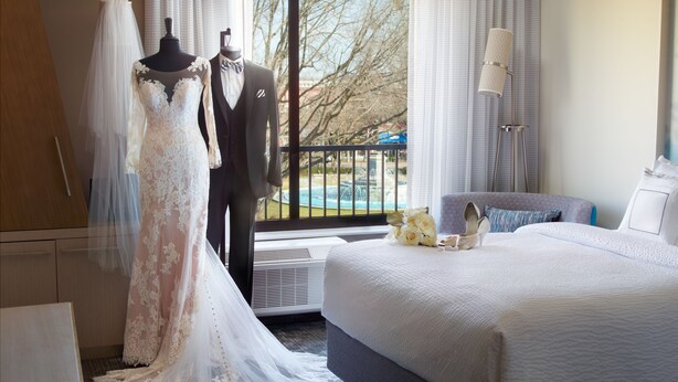 Habitación de hotel con una cama grande, tocador, cómoda y ventana con vistas a árboles y una piscina.