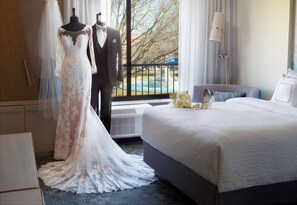 Habitación de hotel con una cama grande, tocador, cómoda y ventana con vistas a árboles y una piscina.