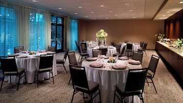 Un salón de banquetes con mesas redondas dispuestas para cenar, ventanas amplias con cortinas y vistas a la ciudad.
