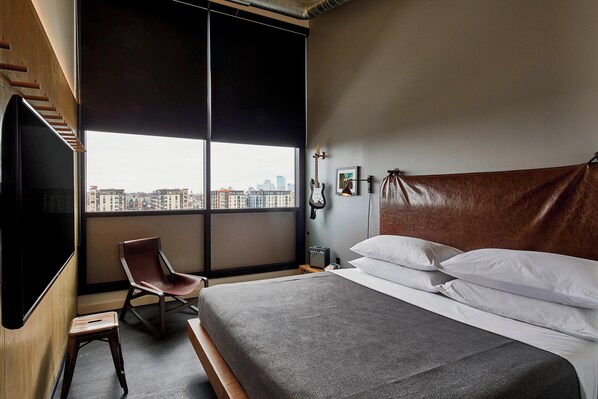 A modern hotel room with a large bed, a chair, a TV, and a city view.
