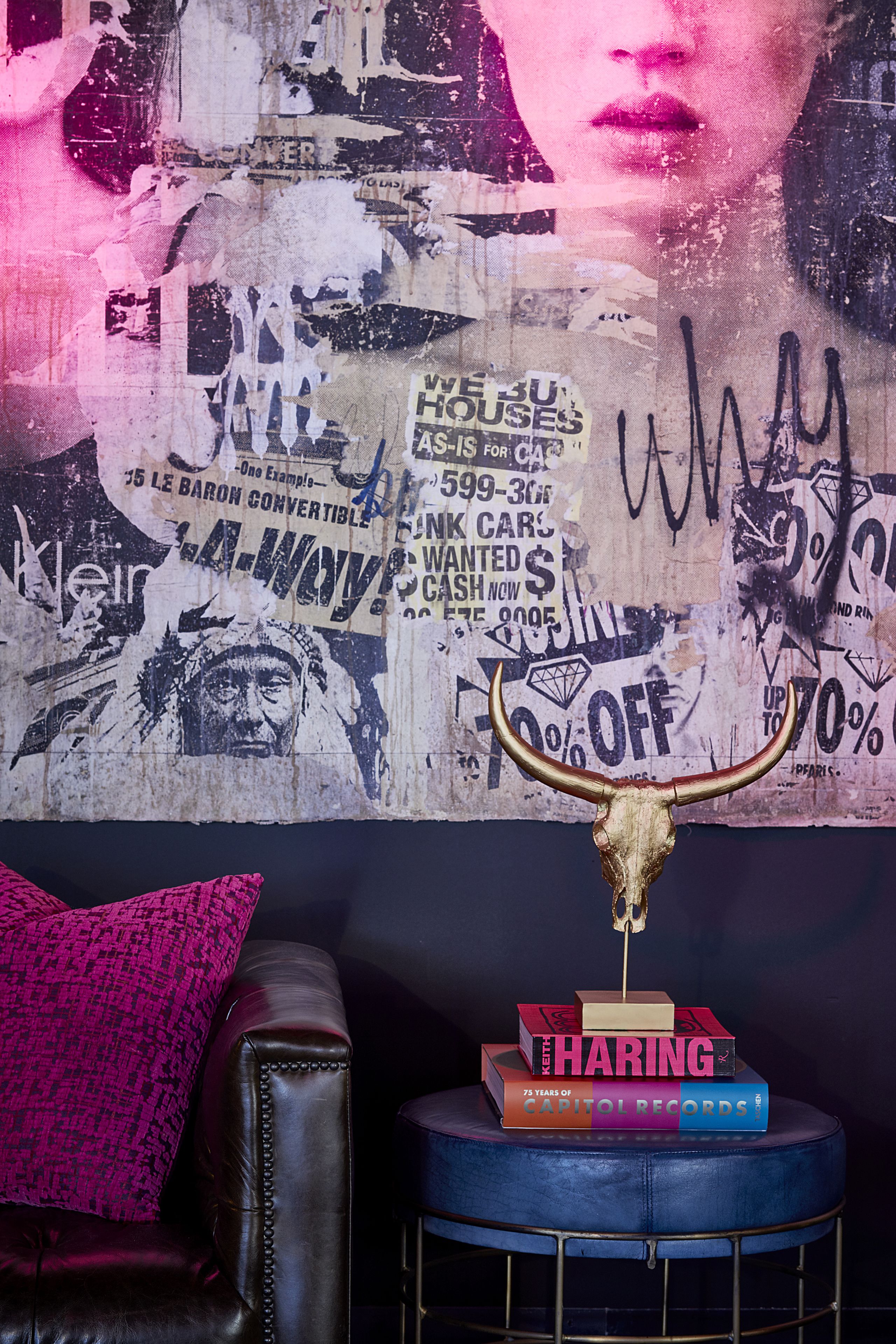 Een kamer met een grote poster aan de muur, een leren fauteuil, een klein rond tafeltje met boeken en een decoratieve stieren schedel.