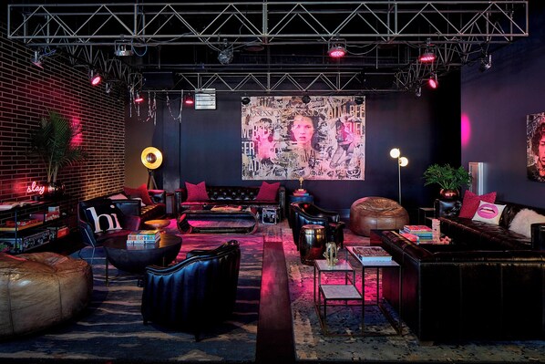 Un área de descanso con pared de ladrillo, sofás de cuero, un gran mural abstracto y una tarima con equipo de iluminación.