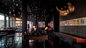 A modern bar area with hanging lights, a large abstract painting, and a brick wall with framed pictures. - MOXY Minneapolis Uptown (Minneapolis)