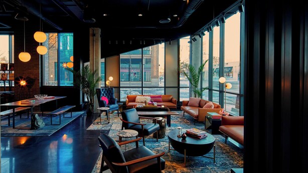 A modern lounge area with seating, tables, and large windows offering city views. - MOXY Minneapolis Uptown (Minneapolis)