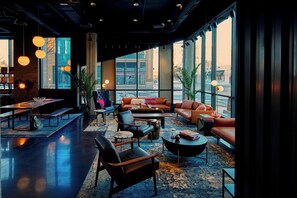 A modern lounge area with seating, tables, and large windows offering city views.