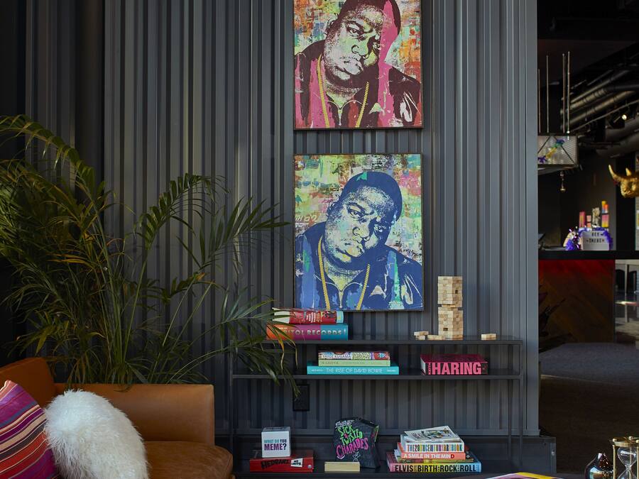 Una sala de estar moderna con una obra de arte grande en la pared, un sofá marrón, una mesa de centro y una estantería con libros y objetos decorativos.