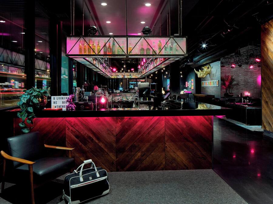 Uma área de bar com balcão vermelho, uma luminária decorativa grande e uma planta.