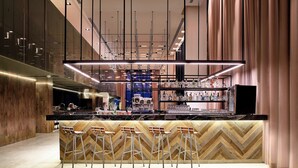 A modern bar area with a herringbone wood pattern wall, bar stools, and a variety of bottles and glasses on shelves. - AC Hotel by Marriott Veracruz (Boca del Río)