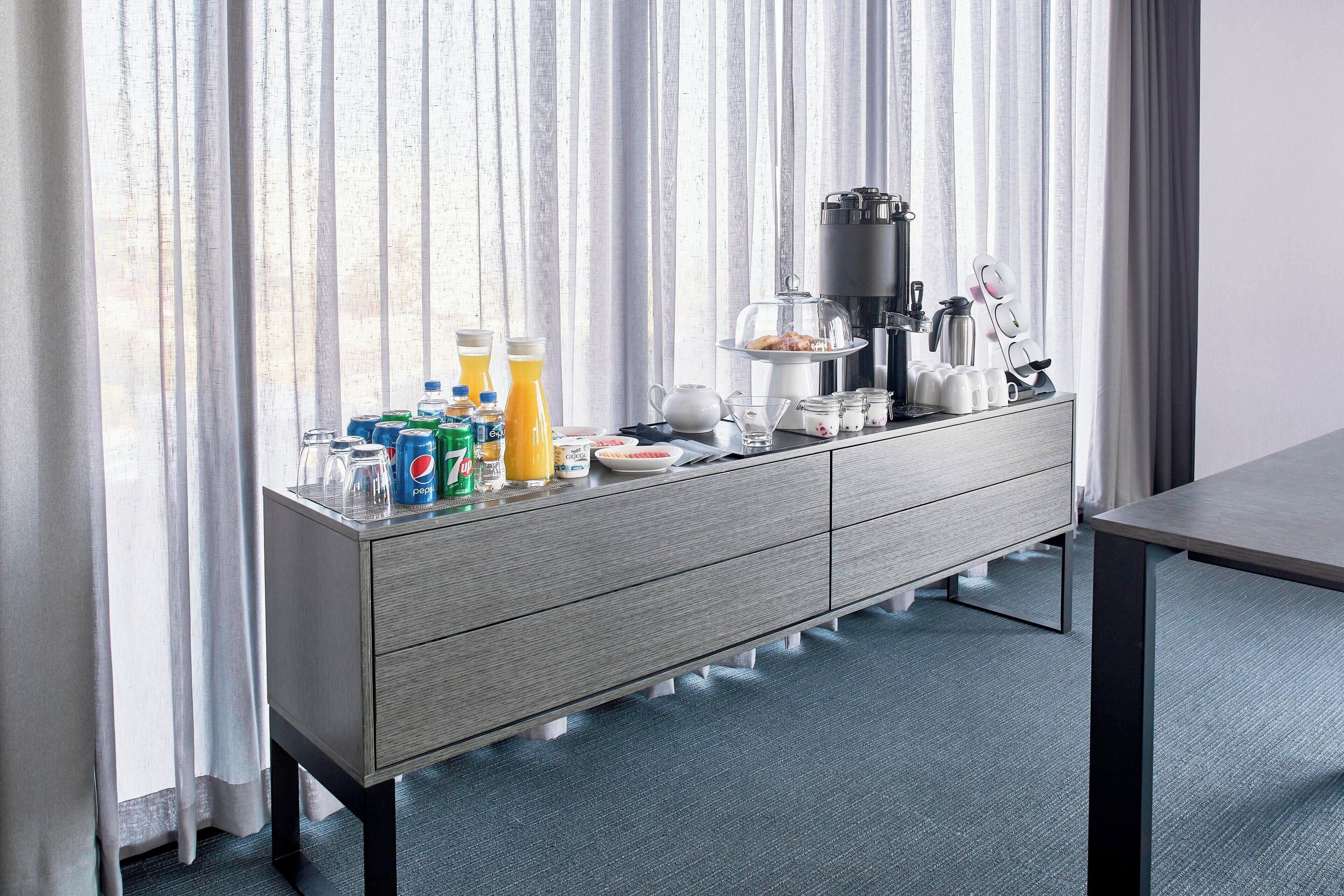 Habitación de hotel moderna con barra de desayuno, cafetera y diversos productos para el desayuno.