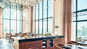 A modern restaurant with a central bar, wooden furniture, and large windows offering a view of the outdoors. - AC Hotel by Marriott Veracruz (Boca del Río)
