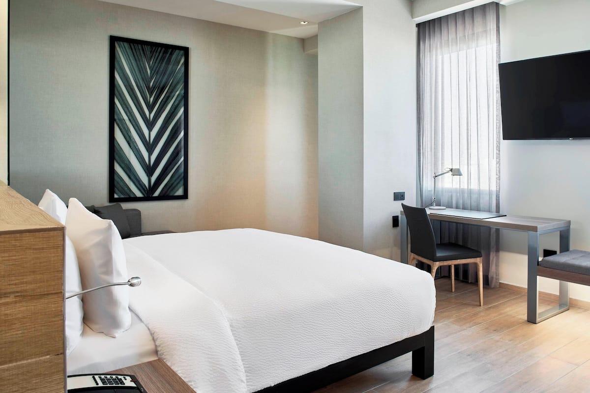 Una habitación de hotel moderna con una cama grande, un escritorio y un televisor.