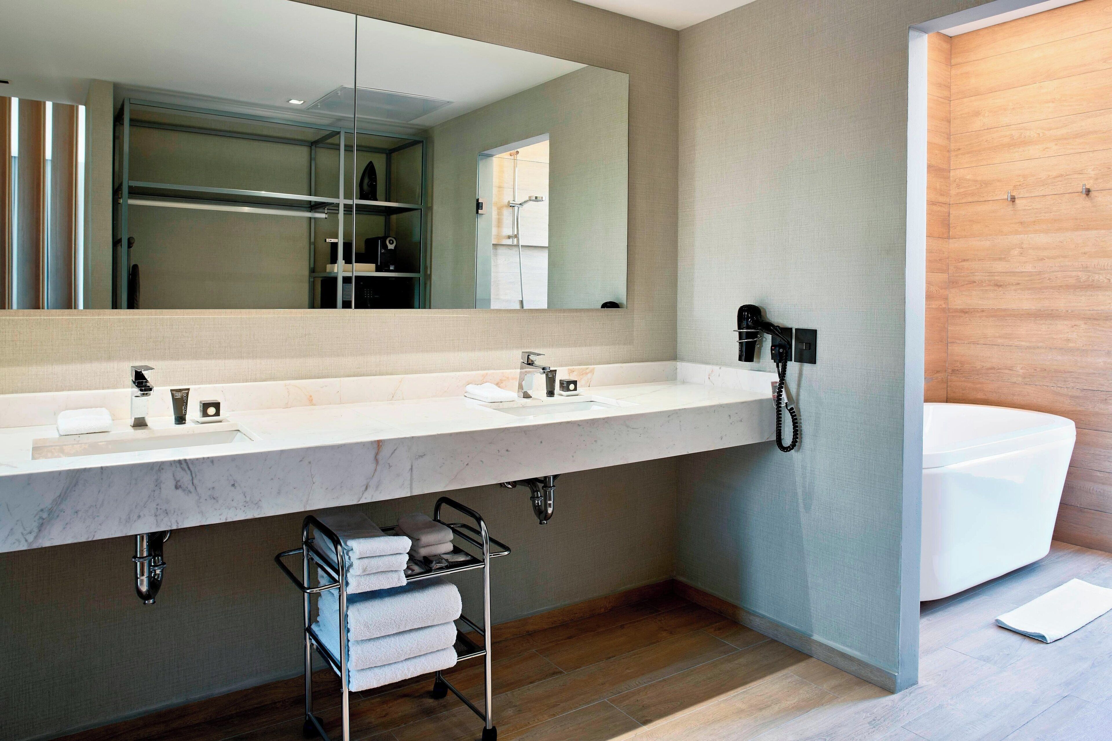 Un baño moderno con un espejo grande, dos lavamanos, un perchero para toallas y una bañera.