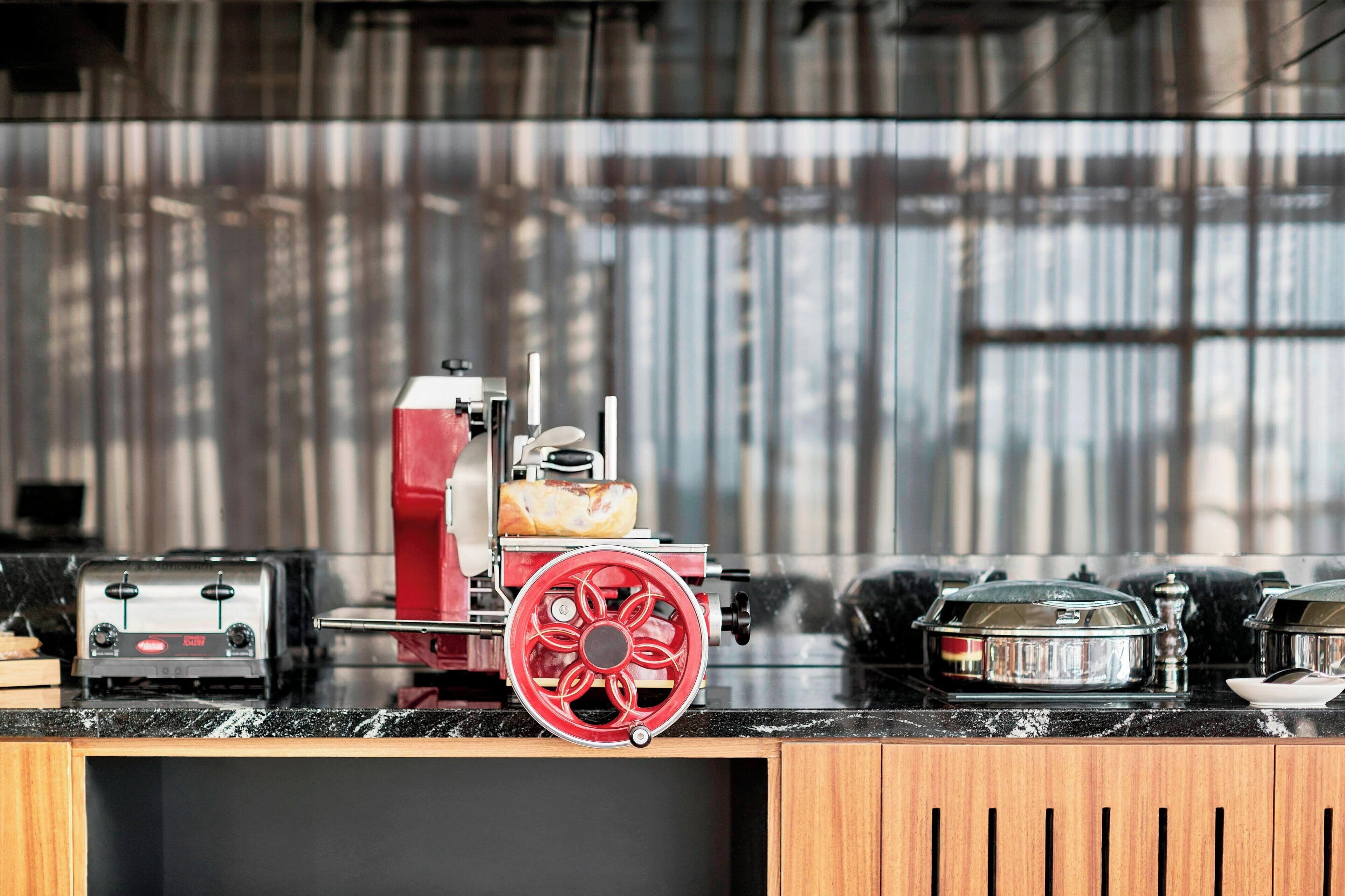 A kitchen with a red meat grinder, a toaster, and a glass container on the counter.