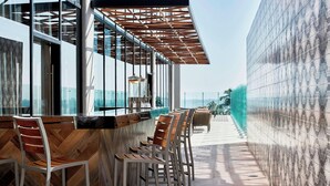 A modern bar area with wooden chairs and a glass railing overlooking a scenic view. - AC Hotel by Marriott Veracruz (Boca del Río)