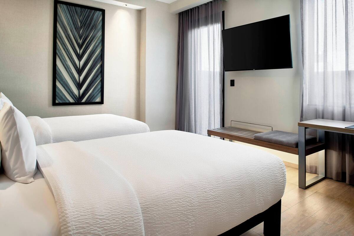 Una habitación de hotel moderna con una cama grande, un escritorio y un televisor de pantalla plana.