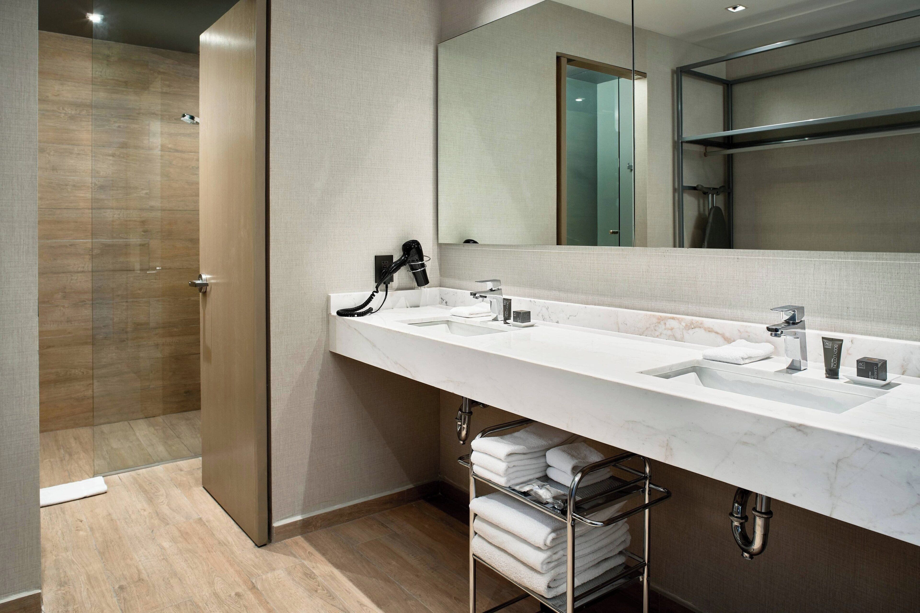 A modern bathroom with a large mirror, two sinks, and a shower area.