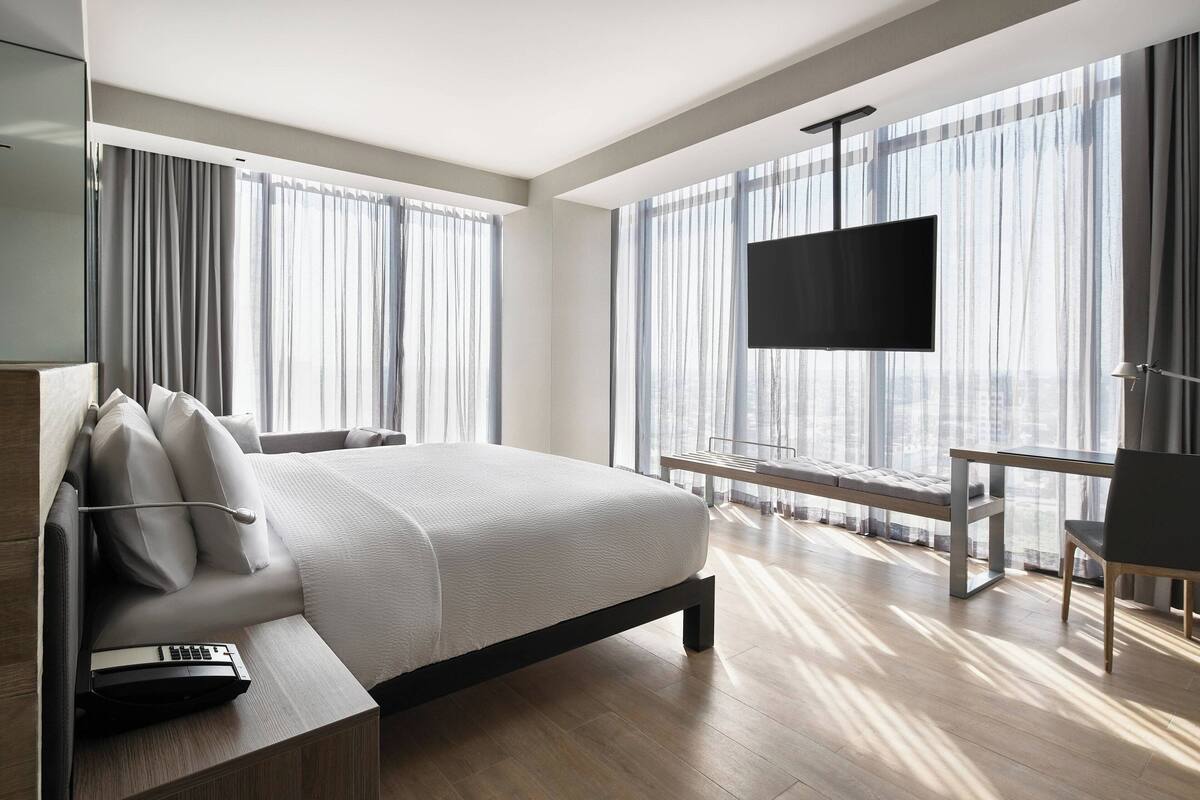 Una habitación de hotel moderna con una cama grande, un escritorio, una silla y un televisor.