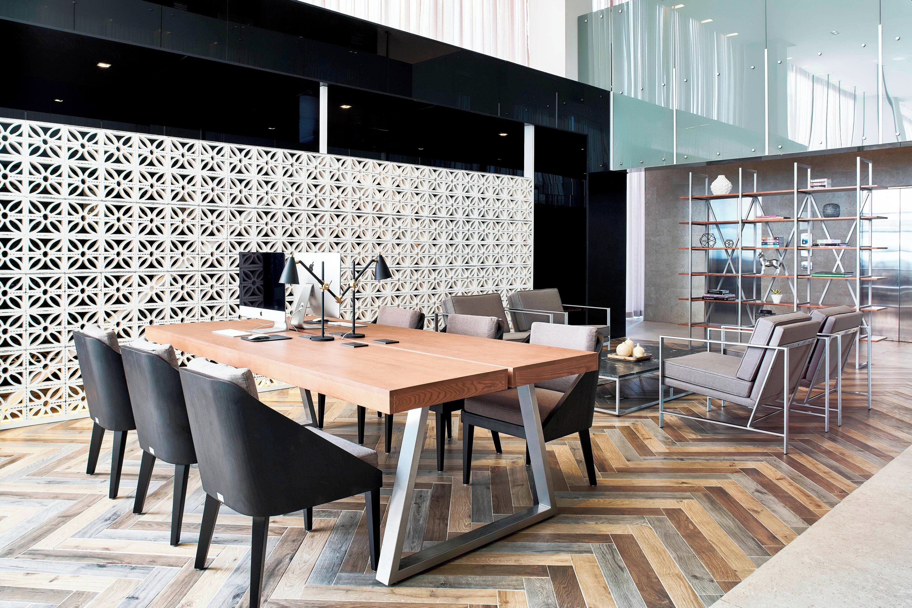A modern meeting room with a wooden table, black chairs, a glass partition, and a metal bookshelf.