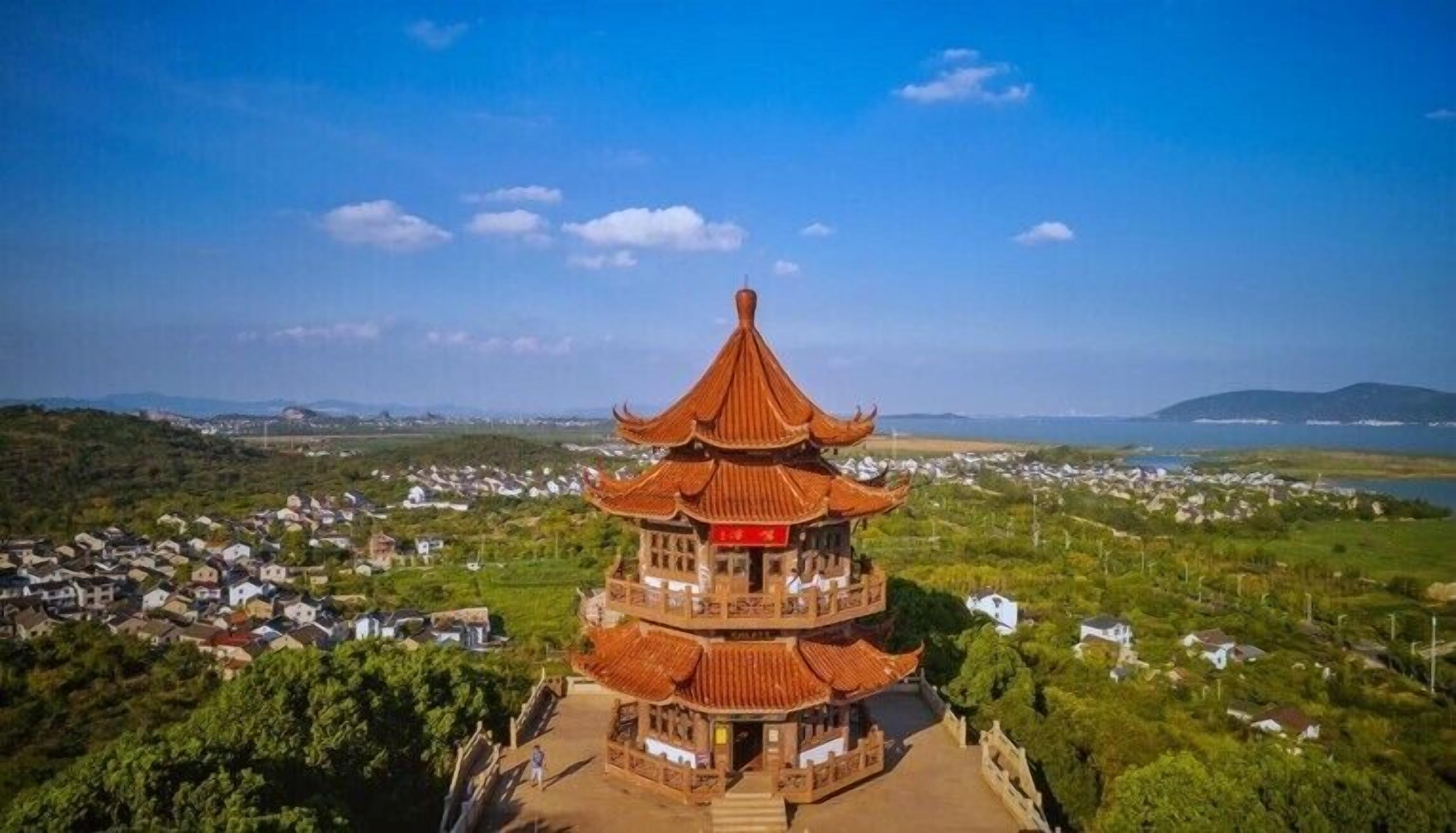 A traditional multi-tiered pagoda with a red roof, surrounded by greenery and a residential area in the background.