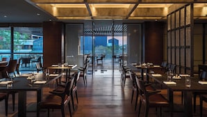 Un espace repas moderne, doté de longues tables et de chaises, de grandes fenêtres et offrant une vue sur l’extérieur.